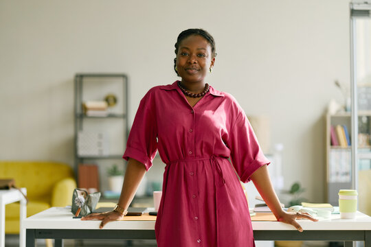 Portrait of young African American businesswoman standing at desk in office, looking at camera and presenting confident leadership. Ideal for workplace branding, career growth campaigns