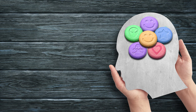 Human Head Silhouette with MDMA or Ecstasy Pills Held by Hands on Dark Wood Surface