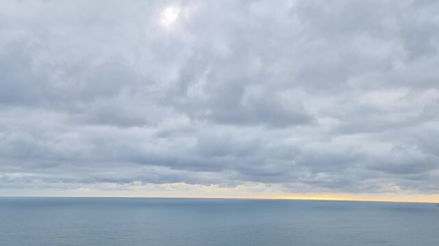Dramatic sunset ocean horizon showcases moving grey clouds over a calm sea during twilight. Stationary wide angle long shot.