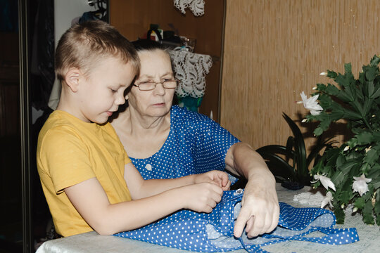 gentle grandmother blue top patiently shows her young grandson how sew piece fabric focused collaboration capturing warmth family learning passing traditions quiet joy creating something together
