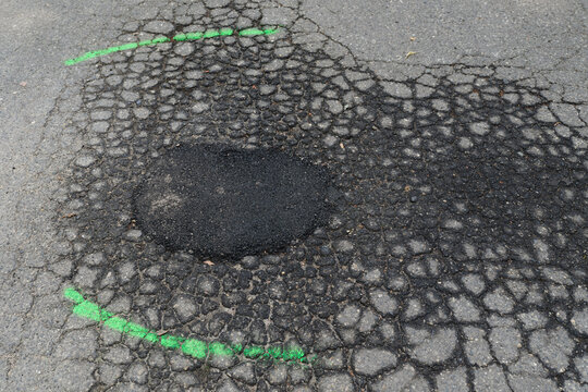 Close up view of damaged asphalt pavement with alligator cracking and a freshly patched pothole marked with green spray paint. Urban road maintenance, infrastructure repair, and street restoration con