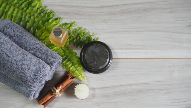 Luxury spa arrangement with gray towels, massage stones, body oil, candle, cinnamon sticks and fresh greenery. Wellness, relaxation, aromatherapy, self care and natural skincare concept with copy spac