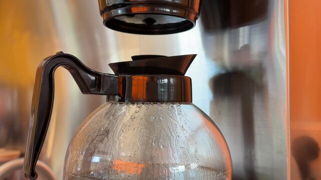 Freshly brewed coffee slowly drips into a transparent glass pot, capturing the simple process of preparing aromatic filter coffee in a professional cafe setting. Close up.