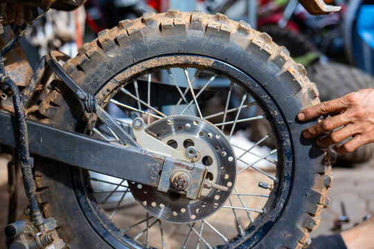 Muddy off road motorcycle wheel with knobby tire being inspected by mechanic hand, gritty workshop scene conveying rugged maintenance and adventure readiness