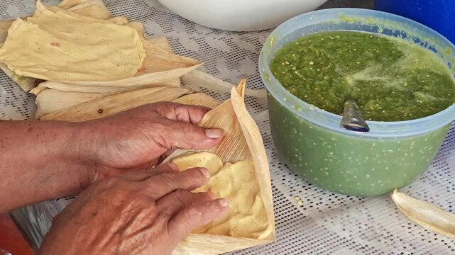 Hands spreading masa dough over dry corn husk for tamale