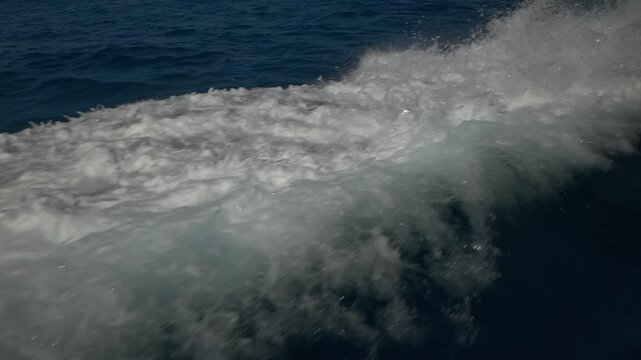 Turbulent white foam water trail behind a large boat in a calm blue sea on a sunny day, slow motion