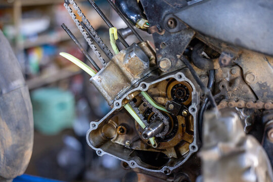 Rusty motorcycle engine crankcase opened for repair with visible camshaft chain guides, gears, oil residue and mechanical components, workshop tools and blurred background conveying focused