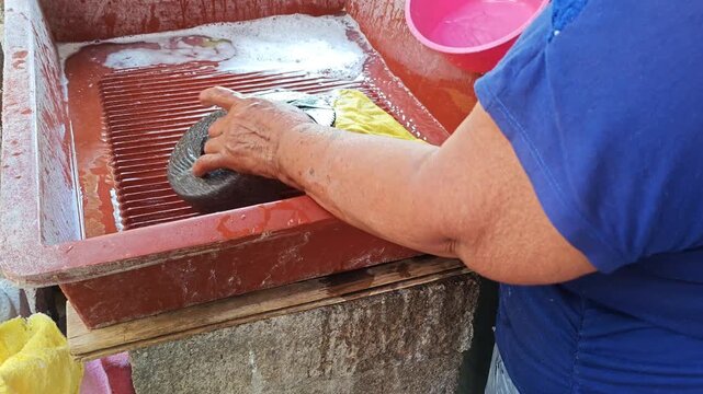 Woman washing traditional millstone tool and cloth outdoors