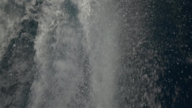 Turbulent white foam water trail behind a large boat in a calm blue sea on a sunny day, slow motion