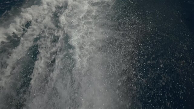 Turbulent white foam water trail behind a large boat in a calm blue sea on a sunny day, slow motion
