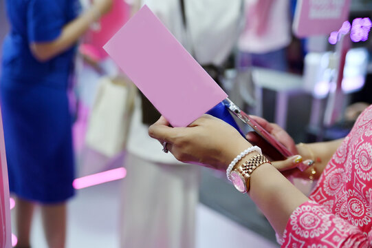 close-up shot of a woman holding a pink card and a smartphone, wearing a watch and a pearl bracelet