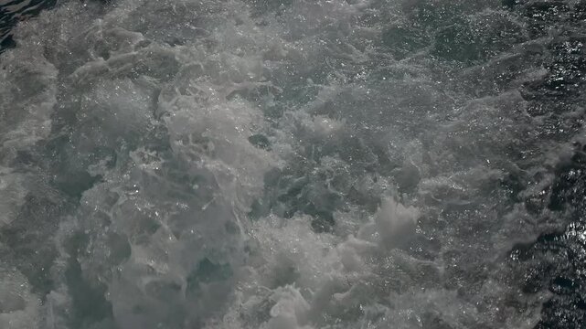 Turbulent white foam water trail behind a large boat in a calm blue sea on a sunny day, slow motion
