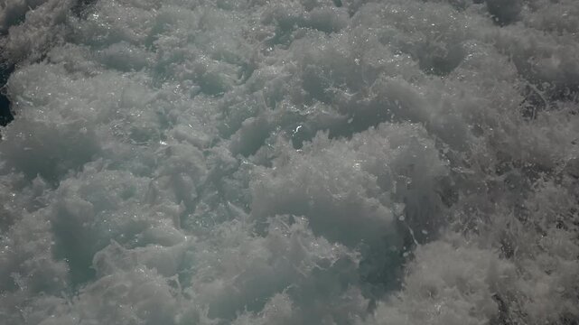 Turbulent white foam water trail behind a large boat in a calm blue sea on a sunny day, slow motion