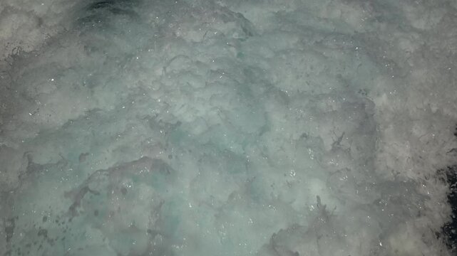 Turbulent white foam water trail behind a large boat in a calm blue sea on a sunny day, slow motion