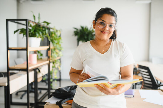 Indian female student holding book smiling in library