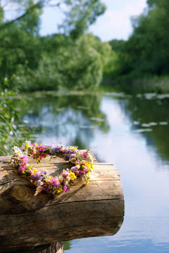 wreath of meadow flowers on tree trunk against river, nature background. beautiful floral decor for Summer Solstice Day, Midsummer, Litha, Ligo Night. pagan witch traditions, wiccan magic ritual
