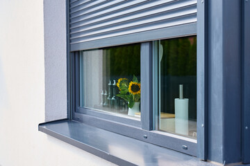 Naklejka na ściany i meble Partially closed exterior roller shutter shades kitchen window with sunflowers and glass bottles inside