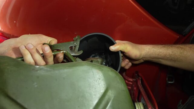 Man pouring fuel from a green jerrycan into a car tank using a funnel.
