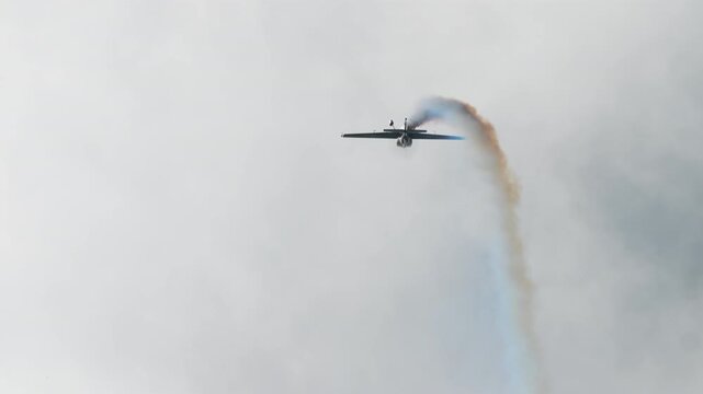 Aerobatic plane arcing over the top of a loop, single engine stunt aircraft curving a smoke trail across a bright sky, sport plane looping at an air show, captured in slow motion