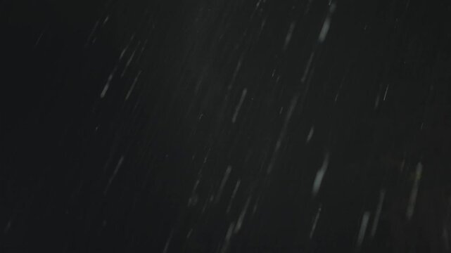 Heavy diagonal rain streaks glow against the blue grey night sky above a dark treeline, a passing flash briefly lights the downpour over the rural countryside