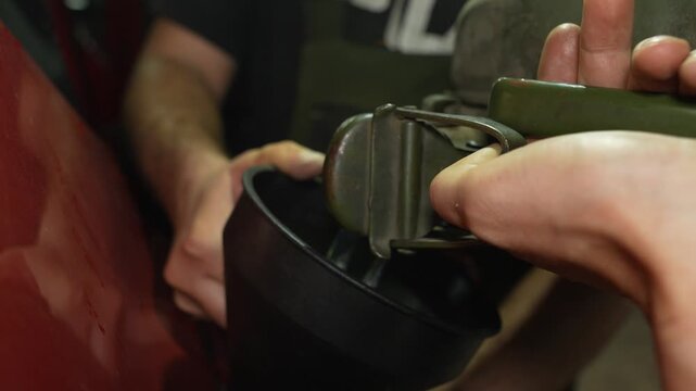 Man pouring fuel from a green jerrycan into a car tank using a funnel.