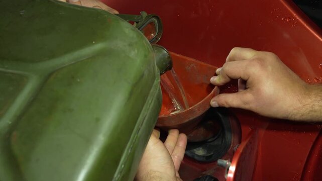 Man pouring fuel from a green jerrycan into a car tank using a funnel.