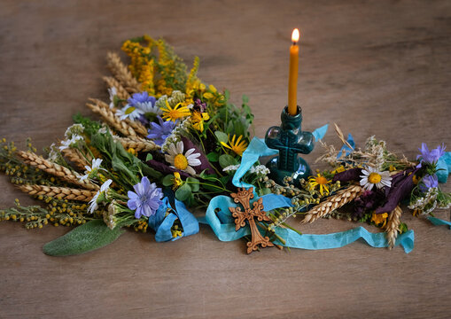 Herbs, flowers tied to sacred bouquet, cross and candlestick on rustic table close up. Herbal consecration - traditional customs on August 15, Assumption of Mary day. christian religion festive ritual