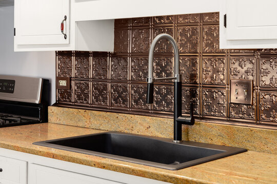 A kitchen faucet detail with white cabinets, a black ceramic sink, and a copper penny tin stamped backsplash.