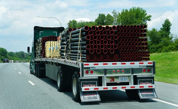 Wilmington, Delaware, U.S.A - Jul 4, 2026 - MaxMiser flatbed semi-truck hauling stacked metal pipes with red ends and wooden crates on highway I-95 North