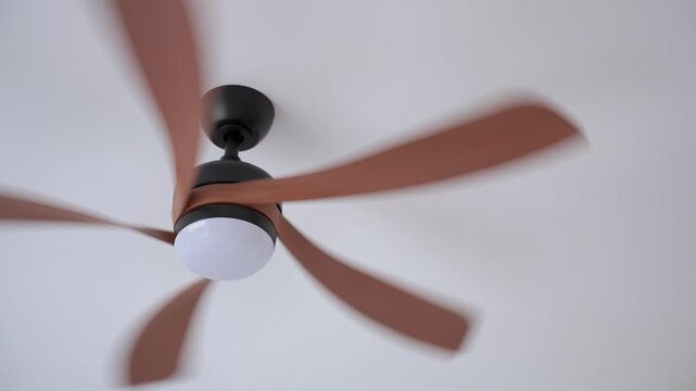 Woman uses remote control to operate ceiling fan mounted on ceiling in modern home. Concept of home cooling and indoor comfort