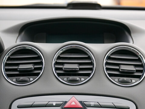 Car dashboard interior with round air conditioning vents. Detail of automobile ventilation system and control panel. Modern vehicle cockpit design and climate control mechanism.
