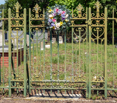 An ornate pair of closed weathered wrought-iron cemetery gates with plastic wreath