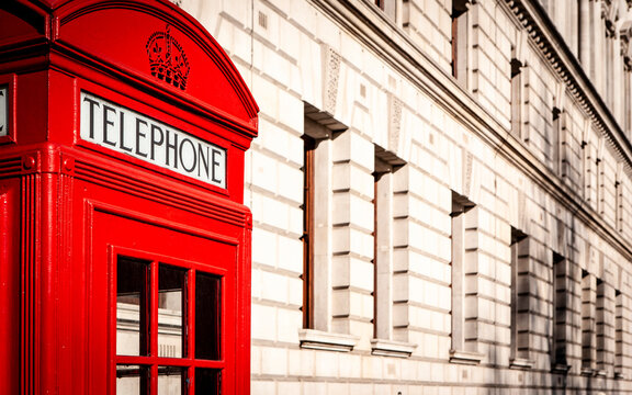 Classic red phone booth in Westminster. Traditional British telephone kiosk positioned beside an ornate historic stone building along Whitehall, London.