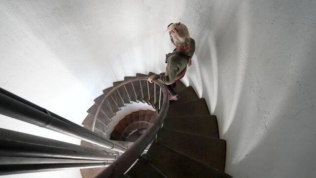 A mature woman walks down the spiral steps of Point Arena Lighthouse in Mendocino California. She moves carefully and steadily.