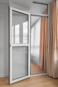 An open white plastic glass door leads to a modern balcony interior with curtains and wooden laminate floor.