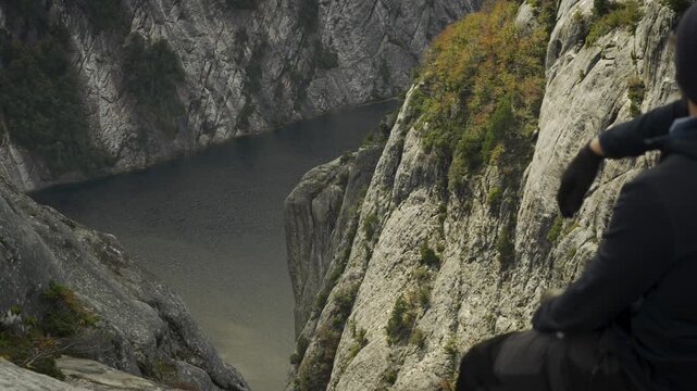 Back view of a hiker sitting on a rocky cliff edge at La Mirada del Doctor viewpoint, overlooking a deep mountain lake and steep terrain in Nahuel Huapi National Park, Argentina.
