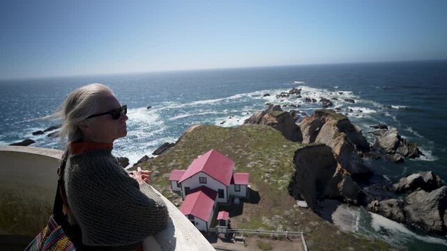 Smiling woman walks around the top of Point Arena Lighthouse while looking out at the Pacific Ocean near Mendocino California