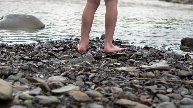 Caucasian child boy walks with his feet on the shore with stones. Children's legs and feet. Vacation, leisure, rest in a mountain river. Happy childhood
