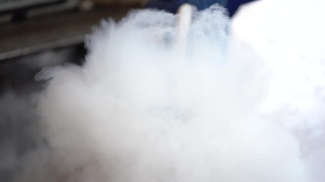 A close-up of an industrial container emitting dense white vapor smoke in a workshop environment.
