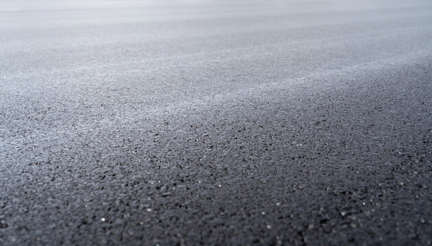 Close-up view of a dark, textured asphalt surface with subtle light variations.