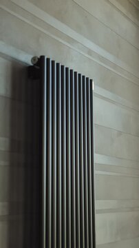 Vertical video. Close-up of a black designer radiator mounted on a modern textured interior wall.