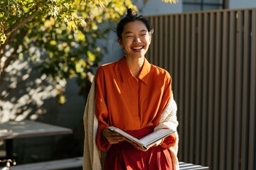 Fototapeta premium Smiling young woman reading book outdoors in sunlit garden setting for lifestyle background and wellness banner design