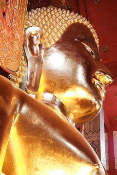 Peaceful face and head of big golden Buddha sculpture with golden reflections.
