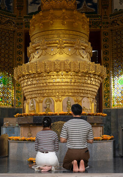 Two Thai Worshippers Kneeling in Prayer Before a Golden Buddhist Stupa Inside a Temple