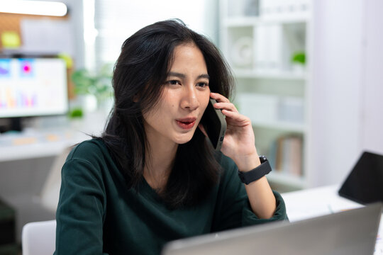 Young businesswoman talking on smartphone while working in modern office. Professional communication, customer service, remote work, and business productivity concept.
