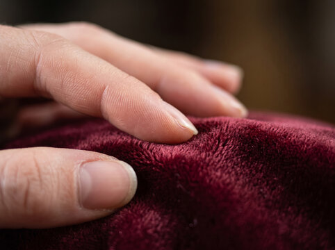 Fingers touching soft luxurious deep red velvet fabric texture closely