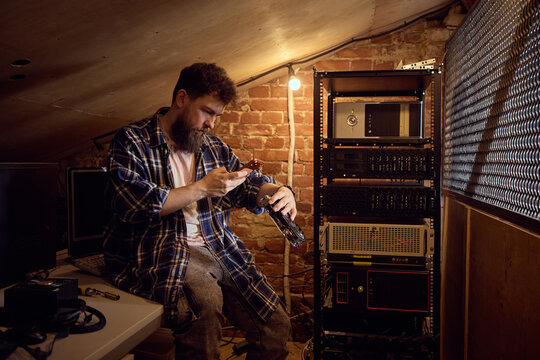 Bearded technician inspecting electronic device from tool bag near server equipment. Concept of hardware replacement workflow, network repair preparation, technical inventory control.