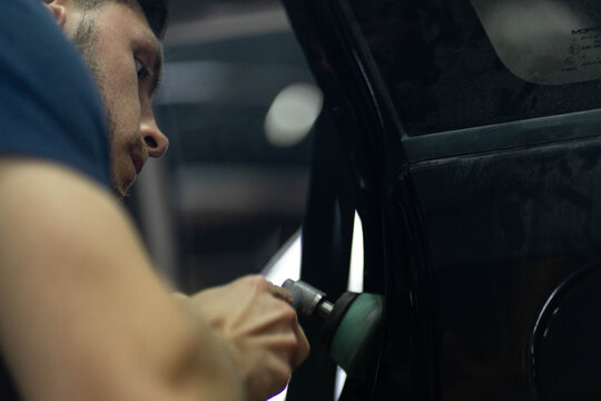 Man polishes vehicle body during repair in workshop. Technician uses professional tool to remove scratches from surface of car door