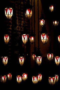 An abstract background of small illuminated hanging lanterns, in red and white leaded stained glass. Cozy and warm decorative evening display.