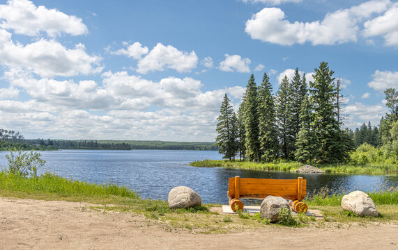 Wooden, Log Bench Overlooking a Peaceful Forest Lake Under Blue Sky; Anglin Lake, Saskatchewan, Canada